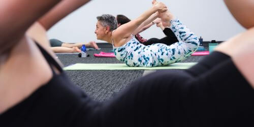 a female yoga student performing a bow pose during a group class