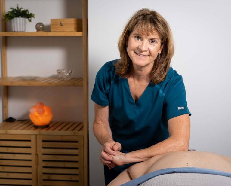 a female therapist massages the back of a client while smiling