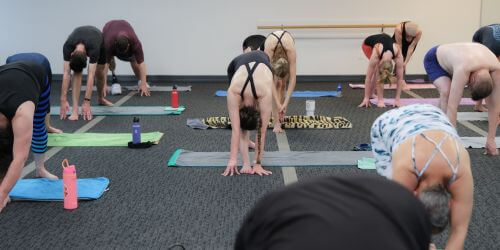 a group of yoga students in a studio performing the Standing Separate Leg Head to Knee Pose