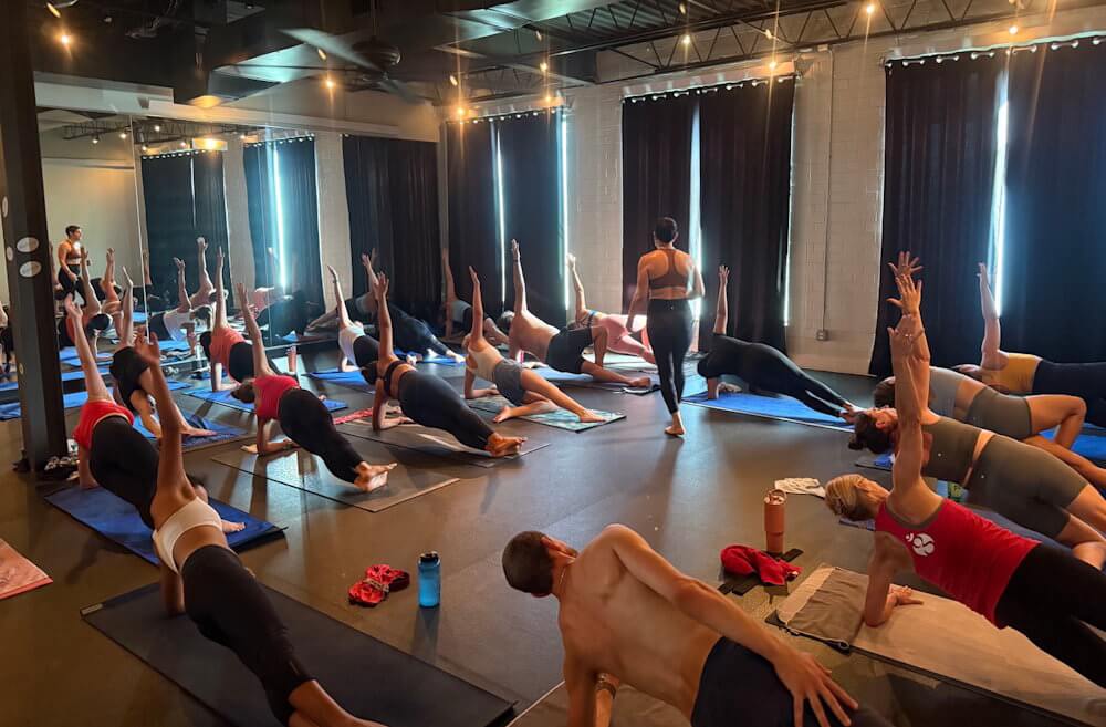 Hot Pilates class with students performing full-body Pilates exercises on yoga mats in a heated studio