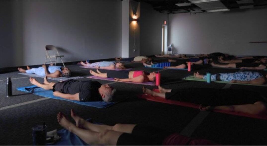 a group of people laying on their back in a dark yoga studio 